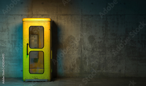 Single old yellow phone booth in retro style standing on the floor in front of the concrete wall at night time. Gloomy poorly lit interior in loft style with copy space. 3D rendering photo