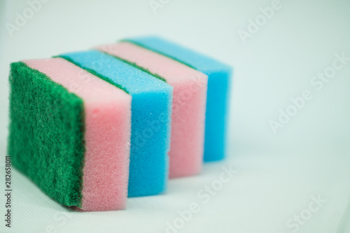 Different color sponges for washing dishes, staggered on top of each other close up on a white background