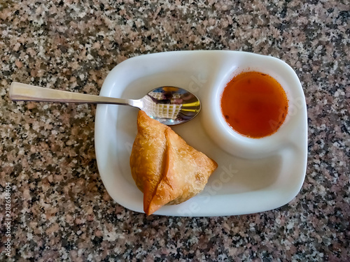 Samosa with chutney or sauce served in a white plate. Top view photo