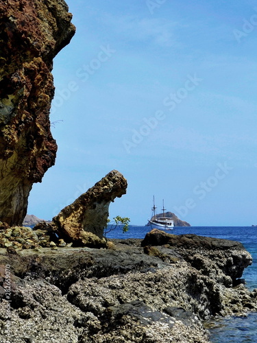 A small ship in the sea on a background of rocky reefs.