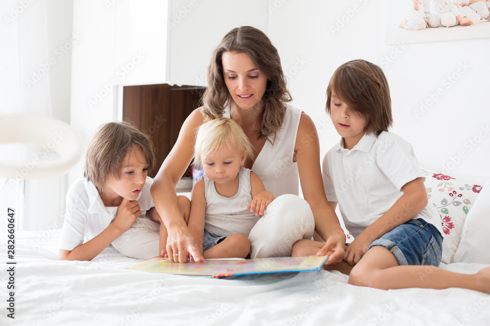 Young mother, read a book to her three children, boys, in the bed Young mother, read a book to her three children, boys, in the bed
