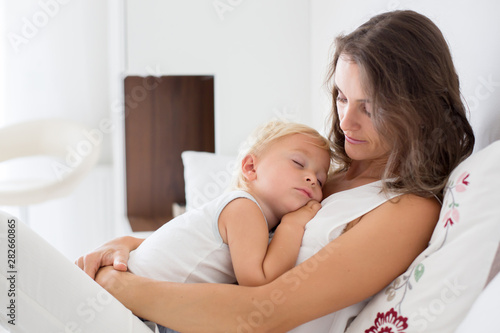 Young mother lying in bed with her sleeping toddler baby boy