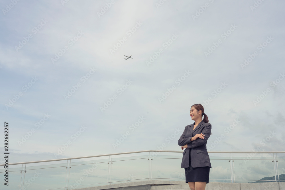 Happy young working woman standing on the top of the building with airplane passing over sky Happy young working woman standing on the top of the building with airplane passing over sky