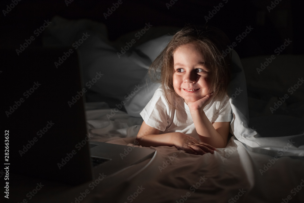 Cute little girl watching cartoon under the covers in bed Cute little girl watching cartoon under the covers in bed