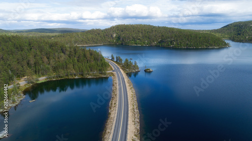 Aerial view of unlimited space of forest plain, highway and lakes. Asphalt road between green fir and pine trees under cloudy sky. Perspective view, summer season in Lapland.