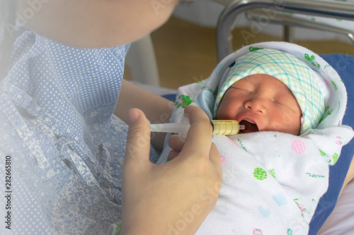 Mother feeding newborn baby milk with syringe