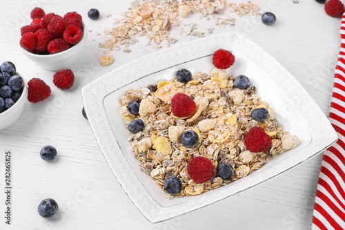 bowl of oat granola, muesli with fresh raspberries, blueberries on white wooden board for healthy breakfast. top view