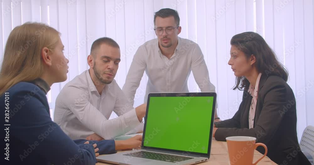 Portrait of four collleagues meeting in the office indoors. Business people using the laptop with green chroma key screen and having a discussion Portrait of four collleagues meeting in the office indoors. Business people using the laptop with green chroma key screen and having a discussion