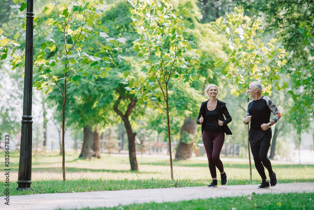 sportive mature sportsman and sportswoman jogging together in park sportive mature sportsman and sportswoman jogging together in park