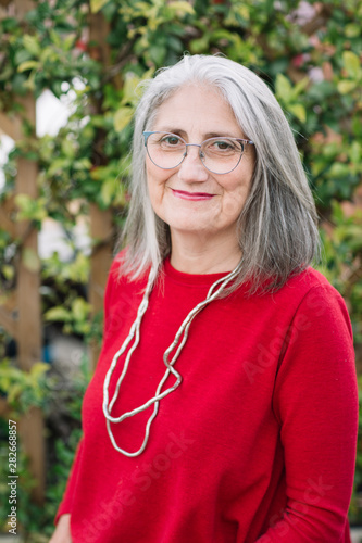 Portrait of smiling senior woman with grey hair wearing red pullover and glasses photo