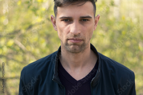 dramatic portrait of a young, brutal-looking man. Close-up. Fashionable hairstyle and manly bristles. Wearing a black leather jacket. The face expresses the “serious intentions” emotion.