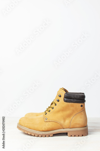 Yellow men's work boots from natural nubuck leather on wooden white background. Trendy casual footwear, youth style. Concept of advertising autumn winter shoes, sale, shop