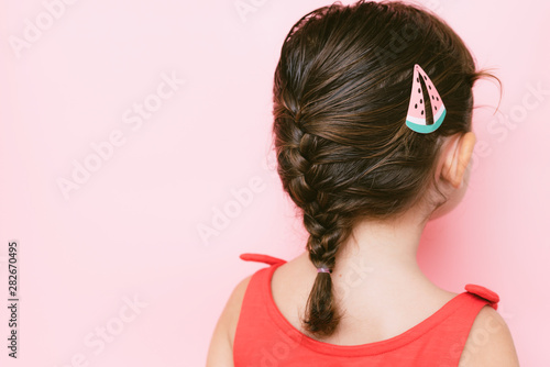 Back view of little girl with braid and hair clip against pink background photo