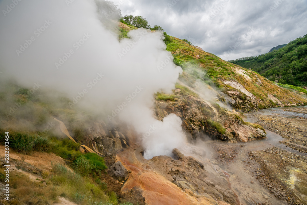 Geyser eruption in the Valley of Geysers in Kronotsky Nature Reserve, Kamchatka Peninsula, Russia. Colorful hill slope of Geysernaya River. Volcanic clay, and geothermal waters surrounding the scene. 