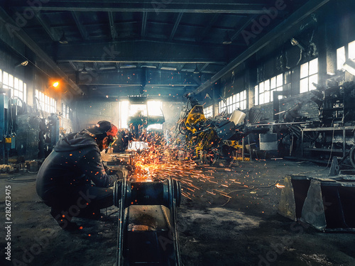 man working with angle grinder metal cutting sparks fly in big hangar