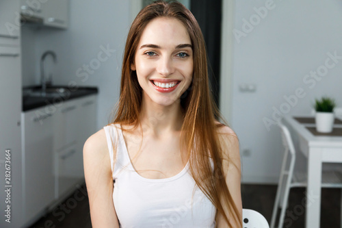 Portrait of adorable smiling young girl sittng at the kitchen and smiling to the camera