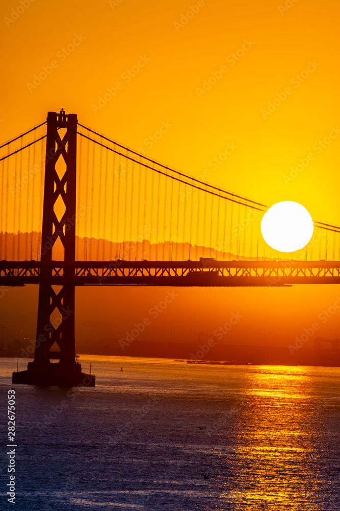 Beautiful summer morning sunrise behind mountain in California gives silhouette to the iconic Oakland Bay Bridge in San Francisco over the ocean.Famous travel location landmark in the west coast city. Beautiful summer morning sunrise behind mountain in California gives silhouette to the iconic Oakland Bay Bridge in San Francisco over the ocean.Famous travel location landmark in the west coast city.