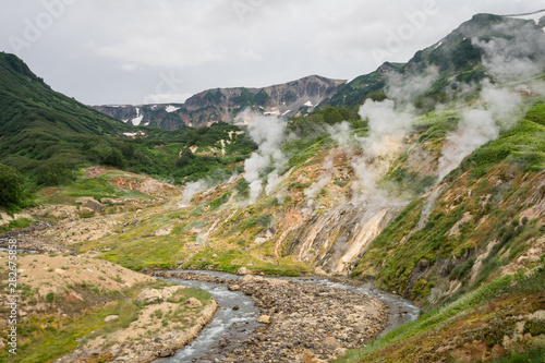 Panorama of the main geyser wall in the Valley of Geysers in Kronotsky Nature Reserve. Slope descending to Geysernaya River, steaming hot springs, mud volcanoes, colorful clay, geothermal waters.