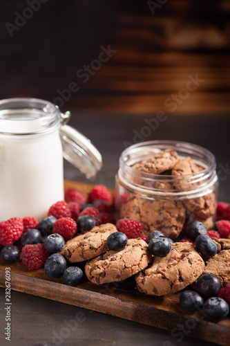Delicious oatmeal cookies with fresh raspberries and milk over rustic wooden table