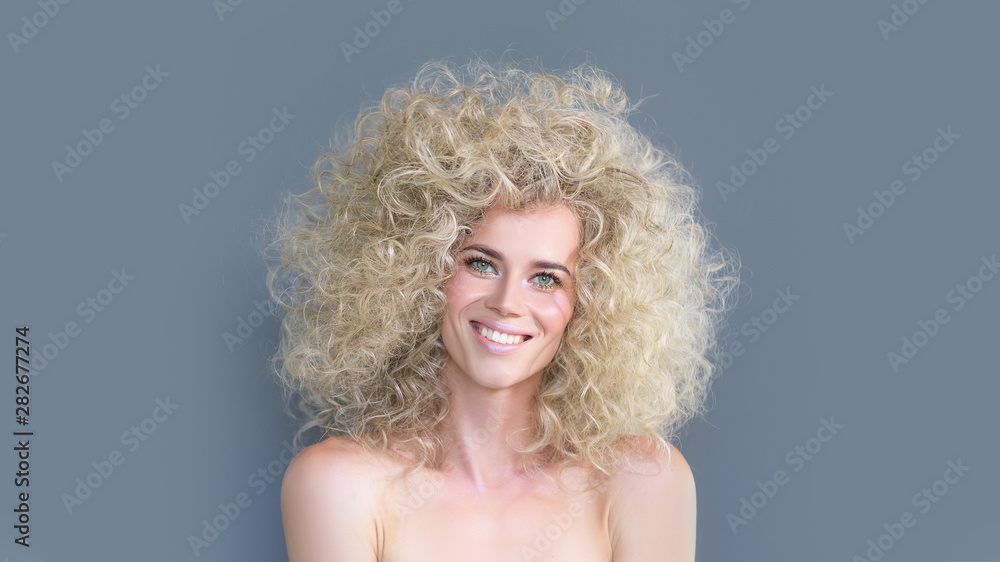 Glad smiling caucasian girl with blond curly hairstyle, laughs happily, expresses sincere emotions, being admired pleased with new haircut, model in studio alone with mockup gray or blue space. 16:9 Glad smiling caucasian girl with blond curly hairstyle, laughs happily, expresses sincere emotions, being admired pleased with new haircut, model in studio alone with mockup gray or blue space. 16:9