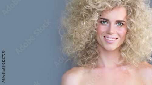 Close-up portrait of a positive charming young blue-eyed blonde girl with curly hair and bright pink delicate make-up. Concept of creating a stylish image. Copy space, 16:9 Widescreen