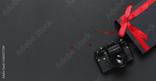 Bild auf Leinwand Old retro vintage camera, Black gift box with red ribbon, confetti on black background top view flat lay with copy space
