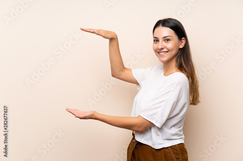 Young brunette woman over isolated background holding copyspace to insert an ad