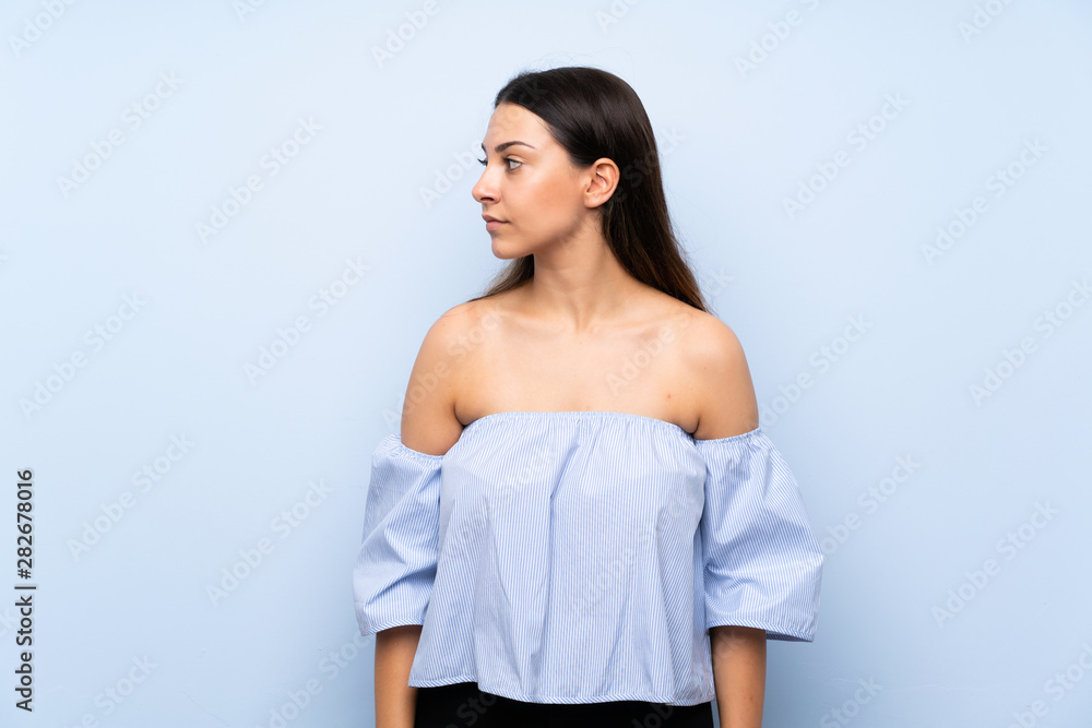 Young brunette woman over isolated blue background looking side Young brunette woman over isolated blue background looking side