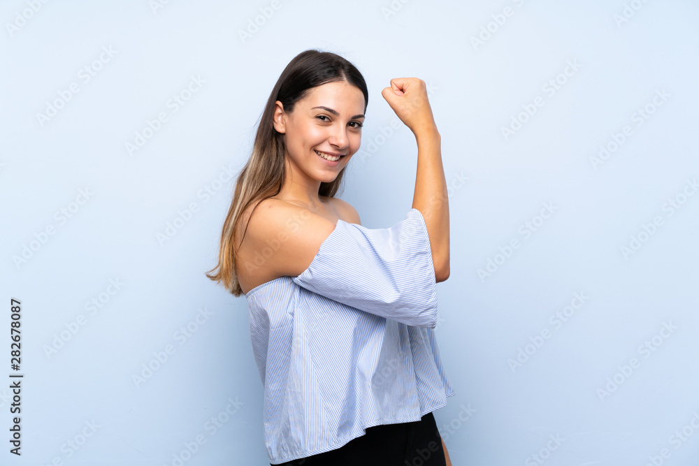 Young brunette woman over isolated blue background making strong gesture Young brunette woman over isolated blue background making strong gesture