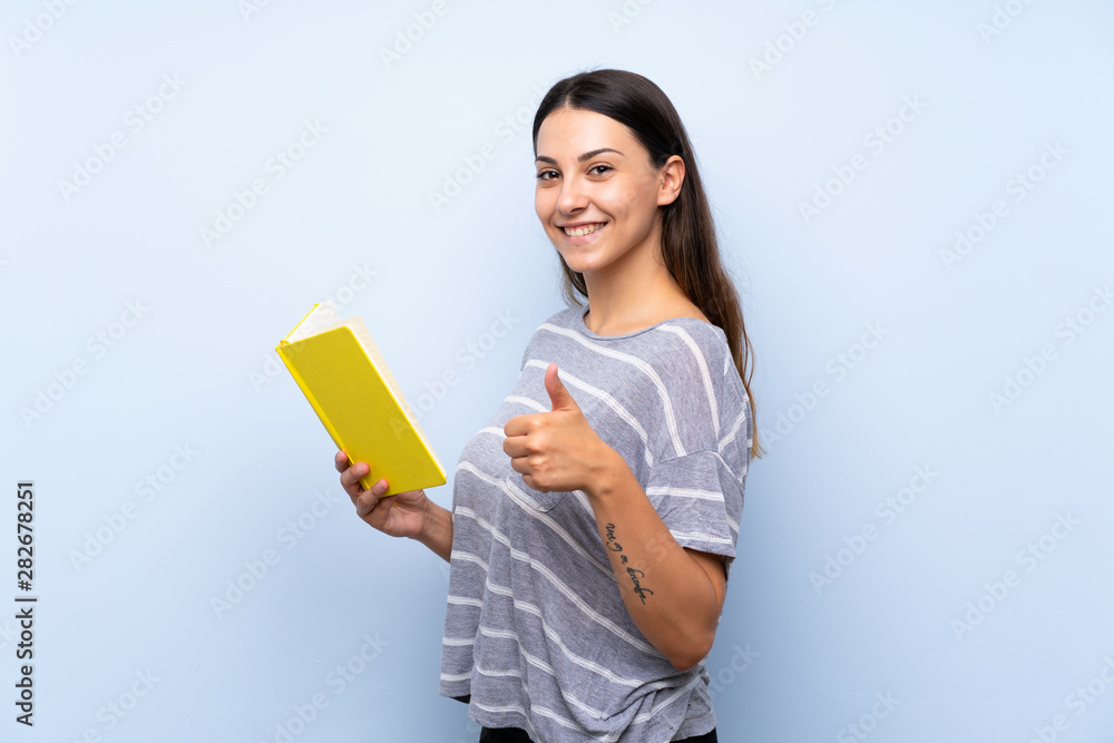 Young brunette woman over isolated blue background holding and reading a book Young brunette woman over isolated blue background holding and reading a book