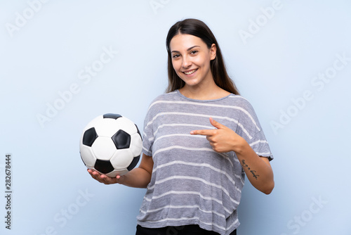 Young brunette woman over isolated blue background holding a soccer ball © luismolinero