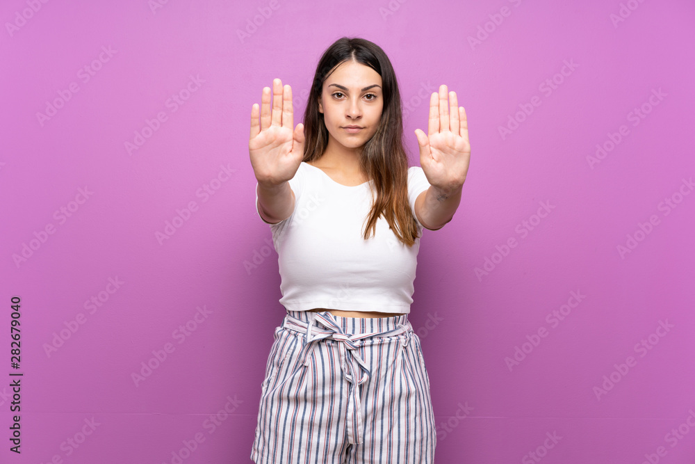 Young woman over isolated purple background making stop gesture and disappointed - obrazy, fototapety, plakaty 
