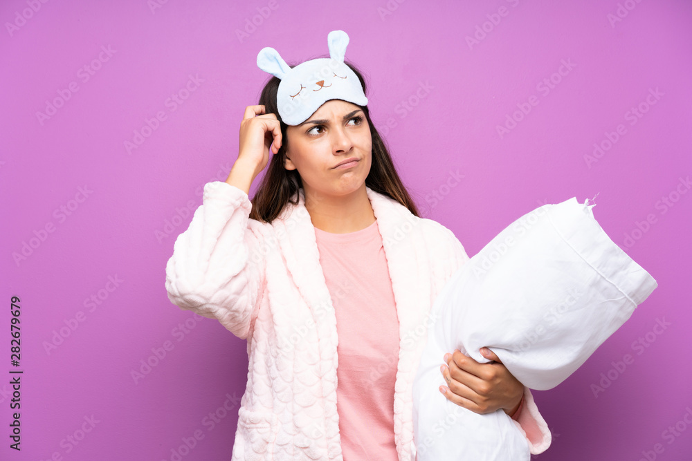 Young woman in pajamas and dressing gown over isolated purple background having doubts and with confuse face expression Young woman in pajamas and dressing gown over isolated purple background having doubts and with confuse face expression