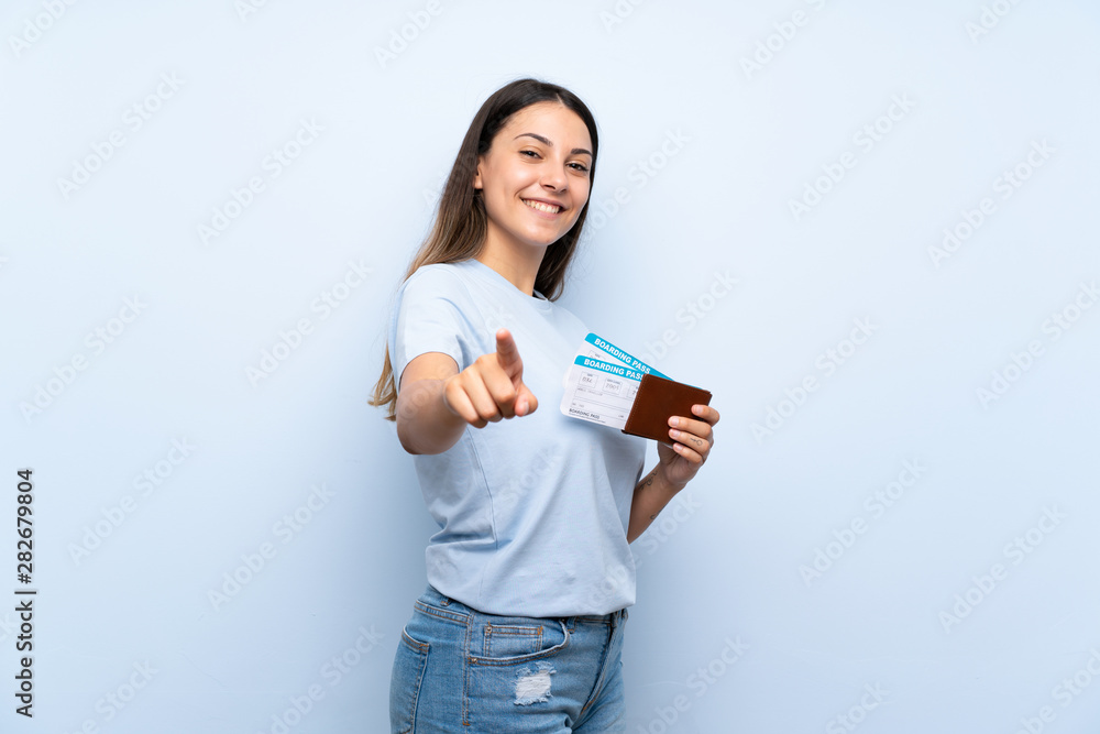 Traveler woman with boarding pass over isolated blue wall points finger at you with a confident expression Traveler woman with boarding pass over isolated blue wall points finger at you with a confident expression