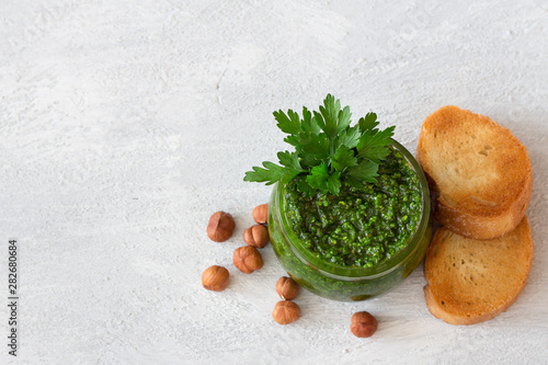 Fresh homemade parsley pesto with hazelnuts in glass jar and bread on light gray background. delicious vegan food. top view, free space