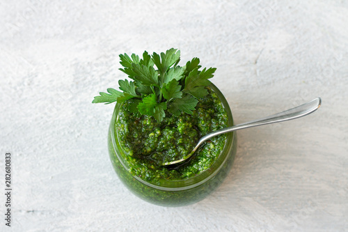 Fresh homemade parsley pesto with hazelnuts in glass jar on light gray background. delicious vegan food