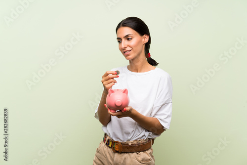 Young woman over isolated green background holding a big piggybank