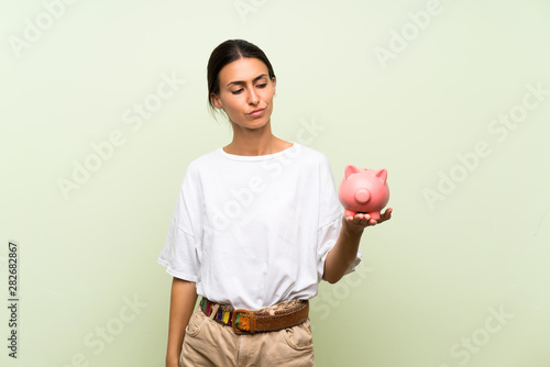 Young woman over isolated green background holding a big piggybank