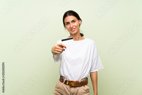 Young woman over isolated green background holding a credit card
