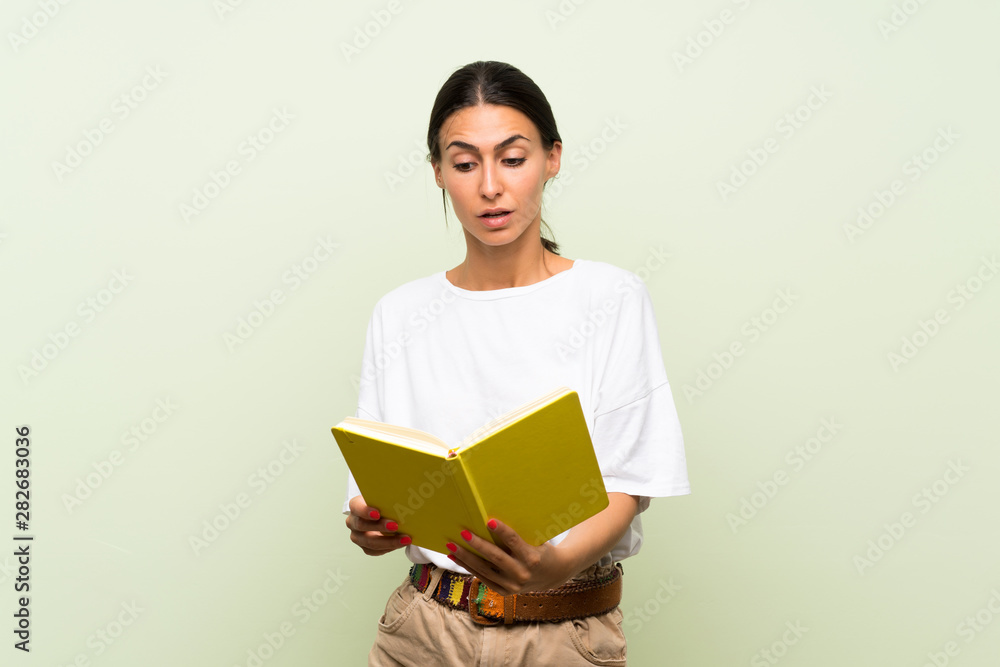 Young woman over isolated green background holding and reading a book Young woman over isolated green background holding and reading a book