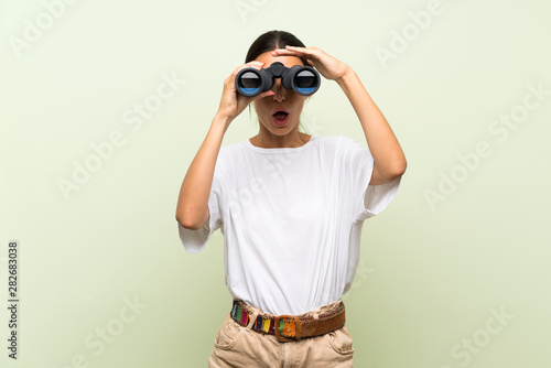 Young woman over isolated green background with black binoculars