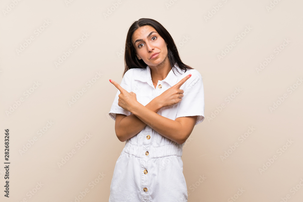 Young woman over isolated background pointing to the laterals having doubts Young woman over isolated background pointing to the laterals having doubts