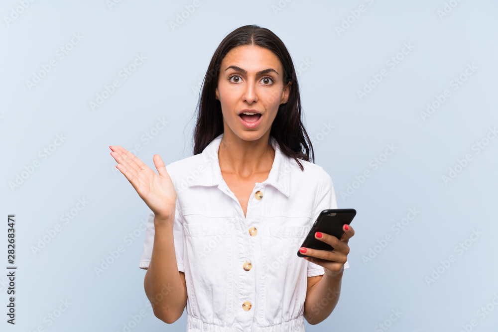Young woman with a mobile phone over isolated blue wall with shocked facial expression Young woman with a mobile phone over isolated blue wall with shocked facial expression