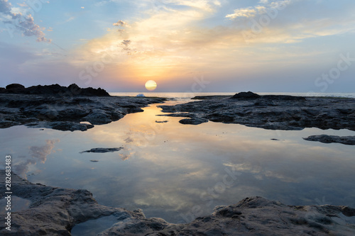 Sunrise at the rocky coast of La Mata near the Spanish port city Torrevieja. The sky is beautifully reflected in the smooth water.
