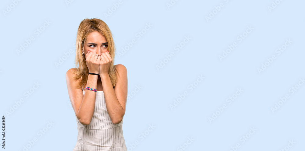 Young blonde woman nervous and scared putting hands to mouth over isolated blue background Young blonde woman nervous and scared putting hands to mouth over isolated blue background