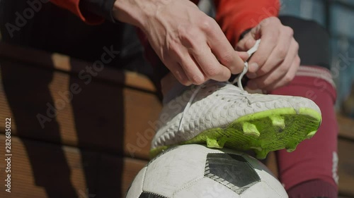Guy tying his shoelaces on soccer shoes on the street. Hands, feet and ball close in sunlight. Stop the soccer ball with your foot. Street football. Slow motion, 4K