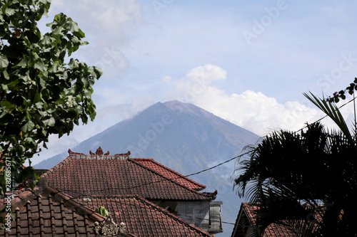 Amed, Indonesia – July 3 2018: The volcano of Mount Agung rises above the rooftops of a village in east Bali, Indonesia