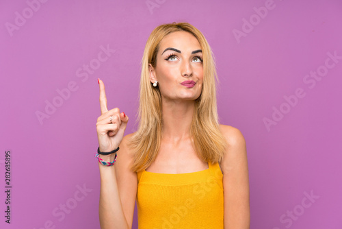 Young blonde woman over purple background pointing with the index finger a great idea