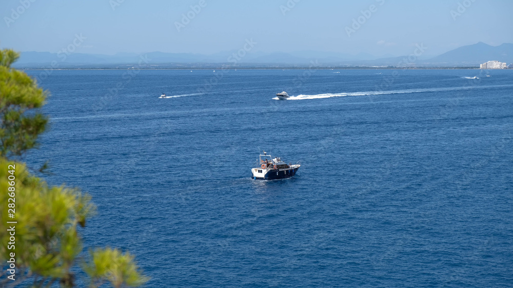 Motor boats sail on the sea on calm water in the sunny day, along the coast of the Mediterranean. Water activities, summer time, happy holidays in the sea concept. Seascape from the mountains.