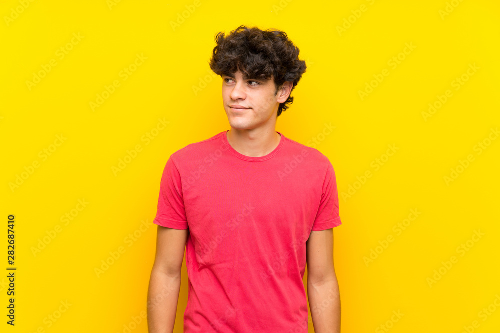 Young man over isolated yellow wall standing and looking to the side Young man over isolated yellow wall standing and looking to the side